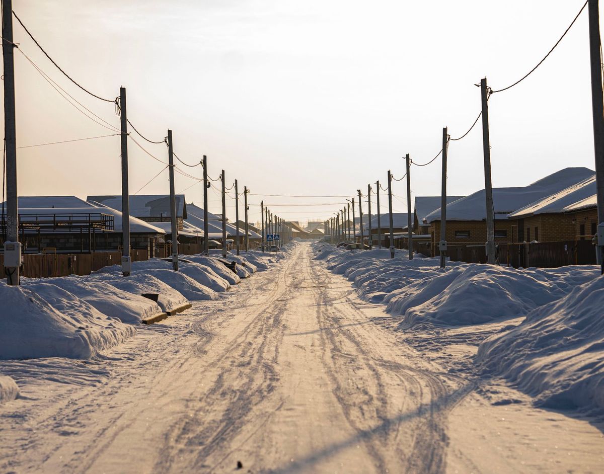 A snow-covered road lined with houses and power lines at sunset